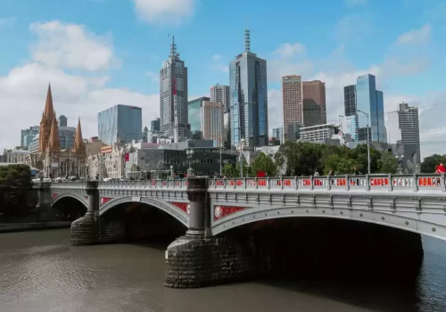 The image depicts the skyline of Melbourne, Australia. Prominent modern skyscrapers are visible in the background, showcasing the city's architectural diversity.